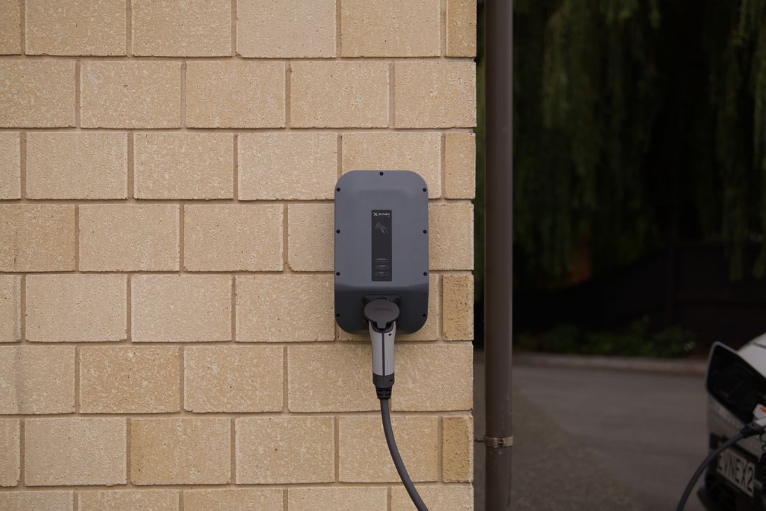 Electrician installing a Level 2 wall-mounted EV charger in a home garage beside an electric car at dusk
